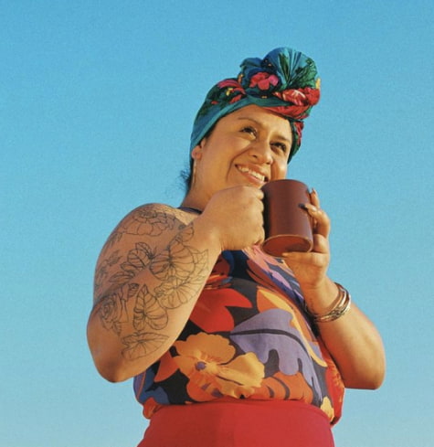 Woman standing against a blue sky holding a mug of mud water