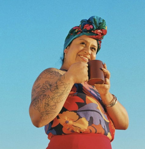 
  Woman standing against a blue sky holding a mug of mud water
